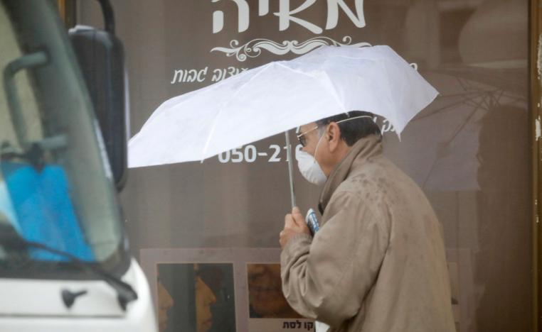 A man walks with umbrella and a mask in Hadera