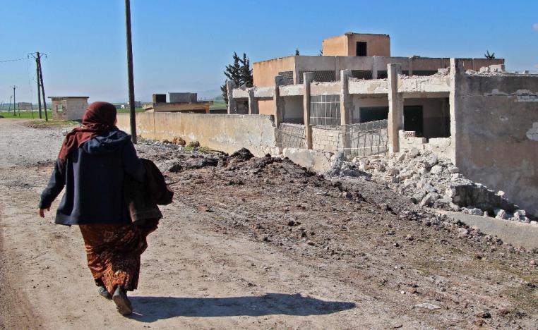 A displaced Syrian woman walks past a school that was reportedly targeted in a regime forces' air strike in Syria's northwestern Idlib province