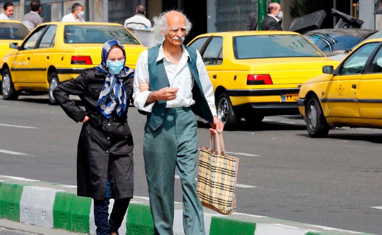 An elderly man and a woman, wearing a protective mask, walk along a street in Tehran