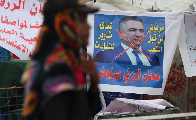 An anti-government protester passes a defaced picture of Iraq's Prime Minister-designate Adnan Al-Zurfi