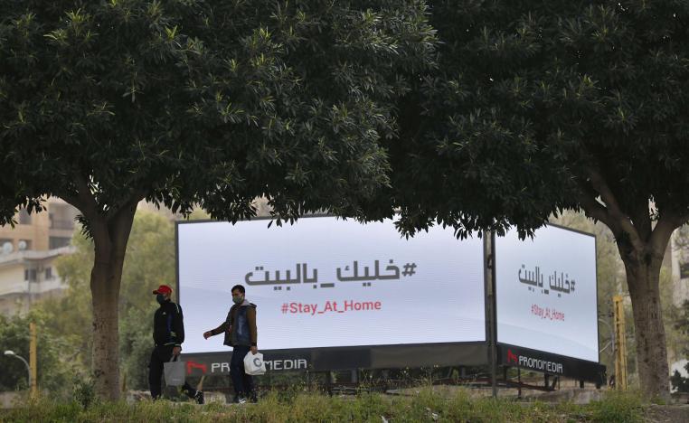 جلان يمران أمام لوحات إعلانية تعرض رسالة تحث المواطنين على البقاء في منازلهم في بيروت