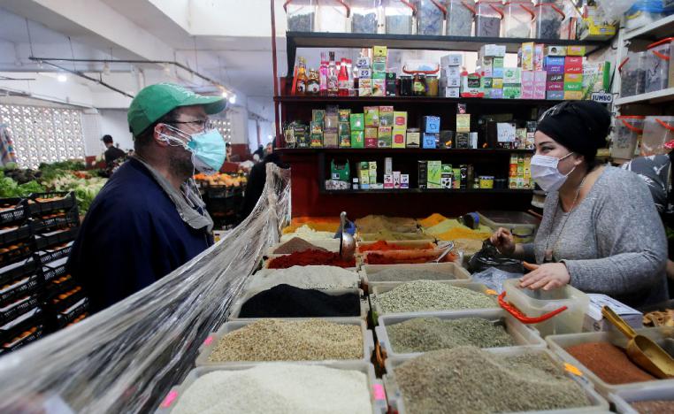 A vendor wearing a protective face mask serves a customer inside her shop in Algiers