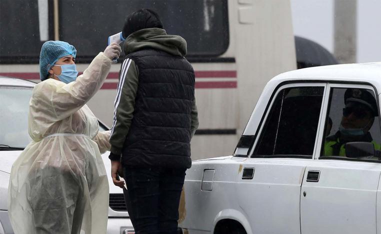 A medical worker in protective suit checks the body temperature of a person at a checkpoint in the city of Vagharshapat