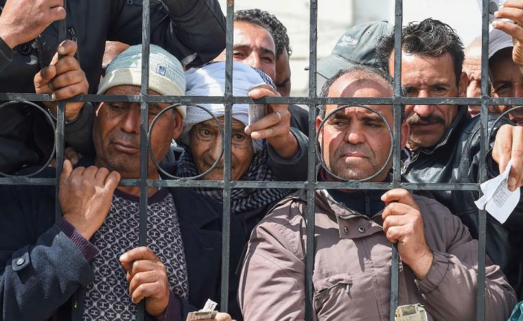 Impoverished Tunisian citizens gather with their ID cards to claim financial aid in Mnihla, Tunisia