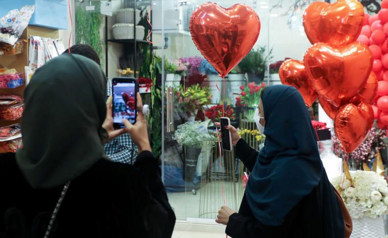 سعودية تلتقط صورة بهاتفها المحمول بينما تحمل امرأة أخرى بالونًا على شكل قلب أثناء تسوقها قبل عيد الحب في الرياض