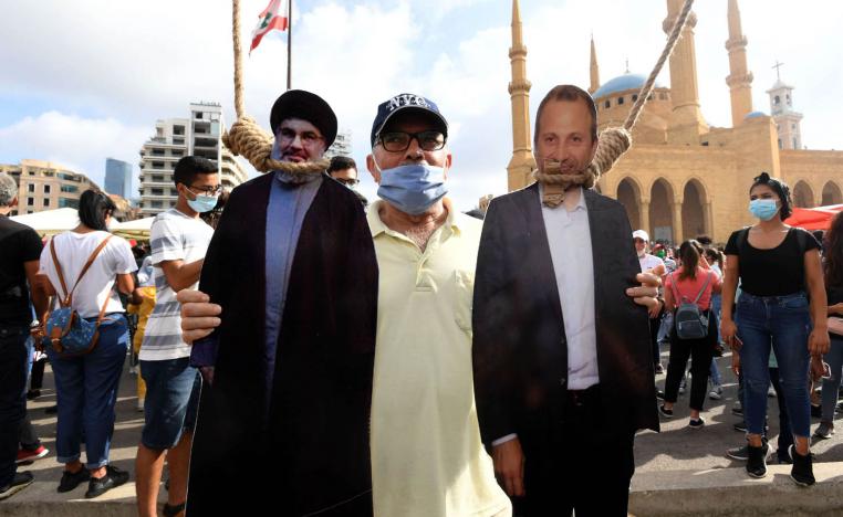 لبناني يرفع صورا معلقة من حبال لجبران باسيل وحسن نصرالله في تظاهرة في بيروت