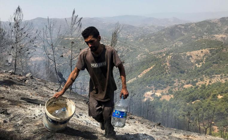 رجل يحمل سطلا وقوارير ماء يحاول استخدامها في اطفاء الحرائق في بجاية - الجزائر