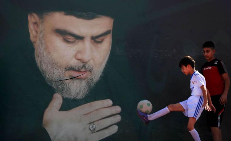 أطفال عراقيون يلعبون بالكرة بالقرب من جدارية لمقتدى الصدر