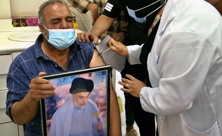عراقي يحمل صورة مقتدى الصدر يتلقى لقاحا مضادا لكورونا