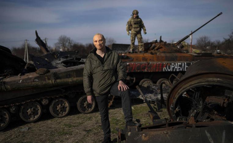 أوكراني يرتدي قناعا لوجه الرئيس الروسي فلاديمير بوتين يقف على حطام دبابة روسية