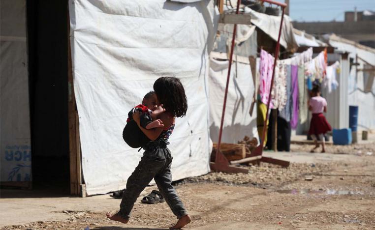 A Syrian refugee girl carries a child as she walks past tents at an informal camp in Bekaa Valley