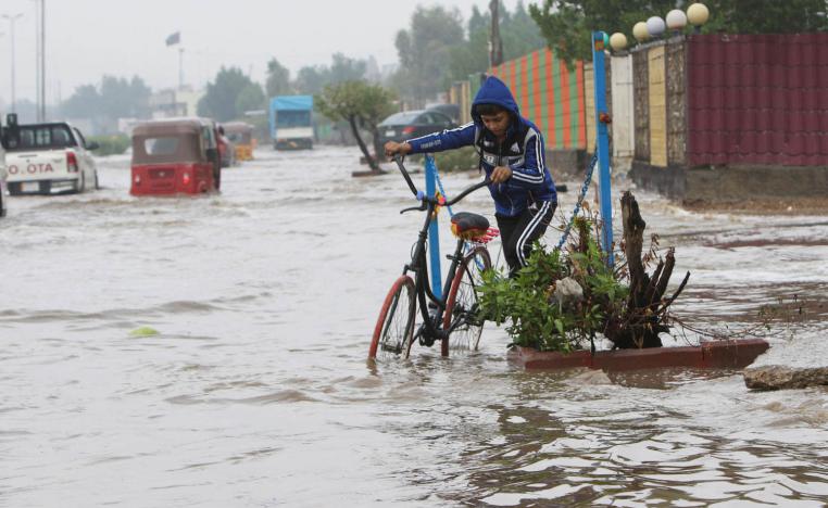 طفل عراقي يحاول تحريك دراجته وسط مياه الأمطار في بغداد