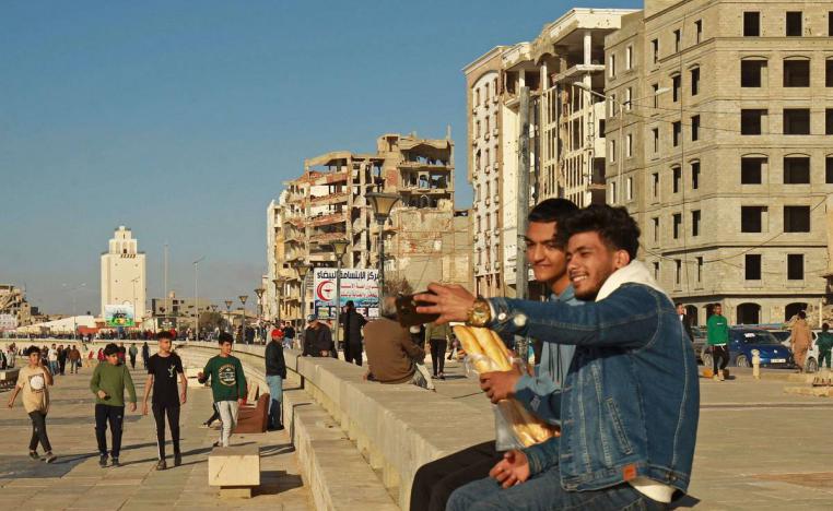 ليبيون على ساحل البحر امام ابنية مدمرة في بنغازي