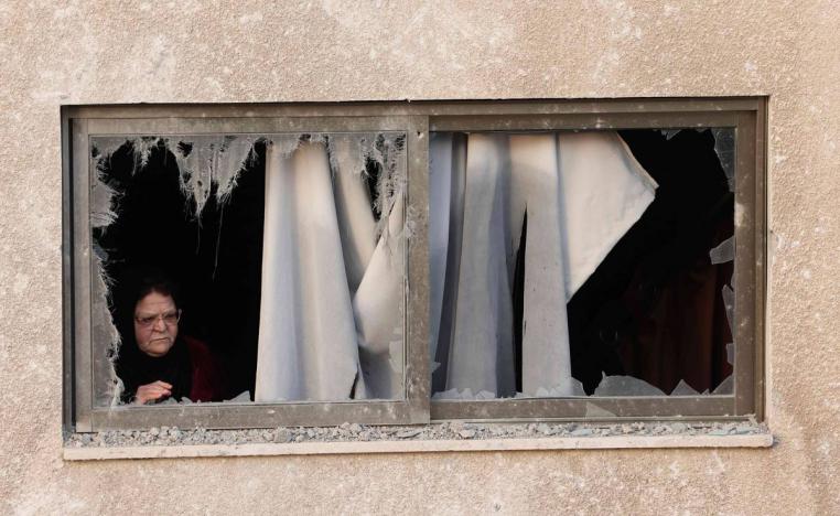 فلسطينية تنظر من زجاج بيتها المحطم على آثار القصف الإسرائيلي في غزة