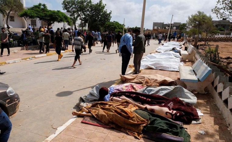 People pass the dead bodies laid on the ground outside the hospital in Derna
