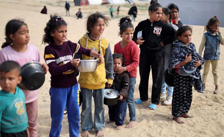 Displaced Palestinian children wait to receive free food at a tent camp amid food shortages