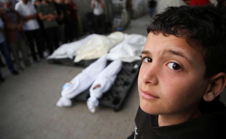 A Palestinian boy stands next to the bodies of Palestinians killed in Israeli strike on Rafah
