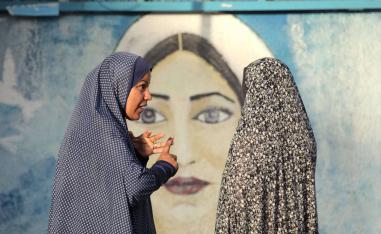 فلسطينيات أمام جدارية للمرأة الفلسطينية في غزة