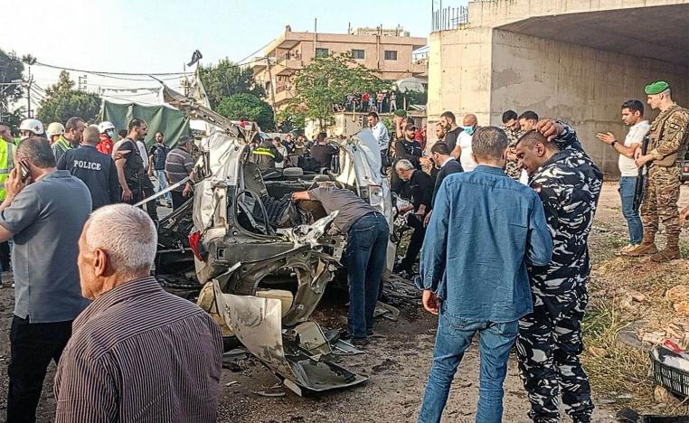 Lebanese army soldiers and onlookers gather around the carcasses of a car after it was hit by an Israeli strike