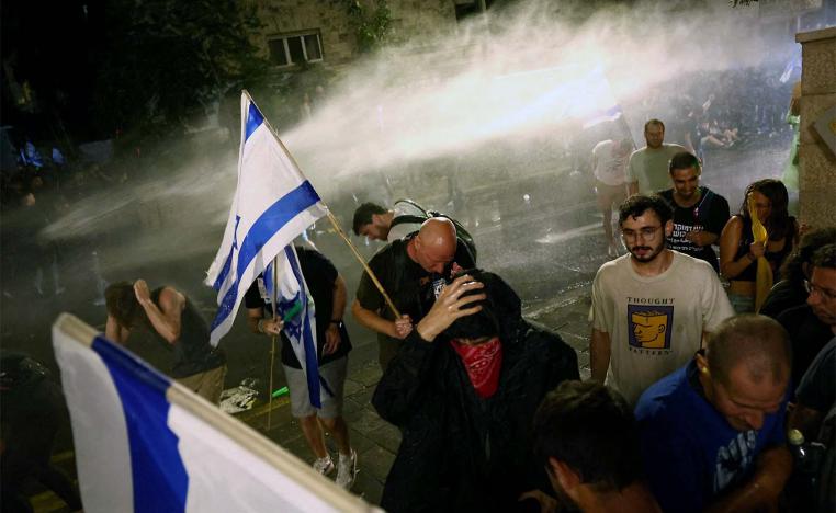 Protesters take cover from a water cannon used from a law enforcement vehicle in Jerusalem