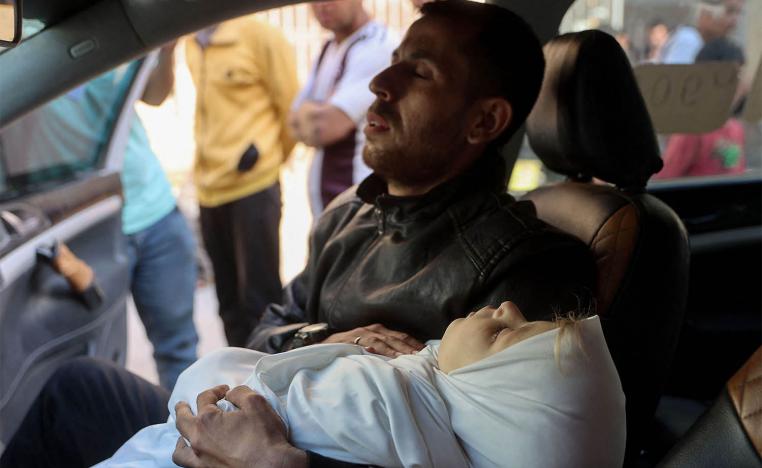A Palestinian man sitting in a vehicle carries the body of a child killed in overnight Israeli airstrikes