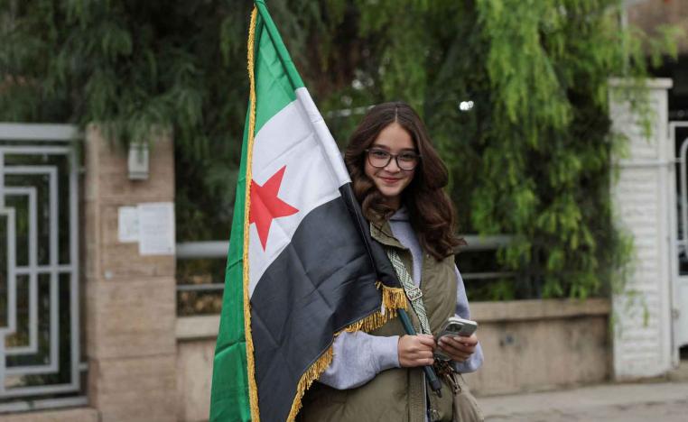 A woman holds a flag on the day of a military parade as Syrians mark the first anniversary of Bashar al-Assad’s fall, in Damascus, December 8, 2025. 