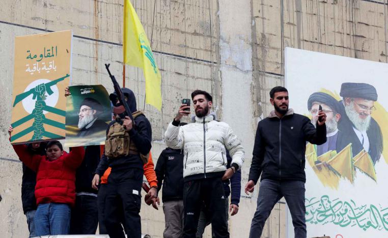 People stand near a poster depicting late Hezbollah leader Sayyed Hassan Nasrallah and late senior Hezbollah official Hashem Safieddine as one of them carries a weapon, in Beirut’s southern suburbs, November 27, 2024. 