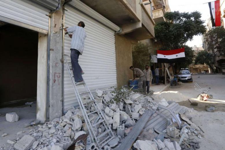 Syrian flags hang from buildings as workers rebuild destroyed stores in Harasta on the outskirt of Damascus, on July 15