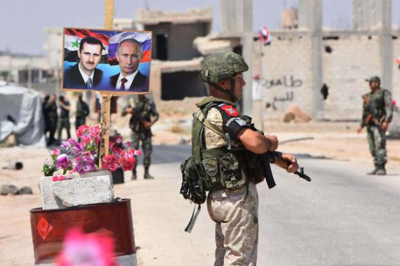 Members of Russian and Syrian forces stand guard near posters of Syrian President Bashar Assad (L) and his Russian counterpart Vladimir Putin at the Abu Duhur crossing on the eastern edge of Idlib, last August.