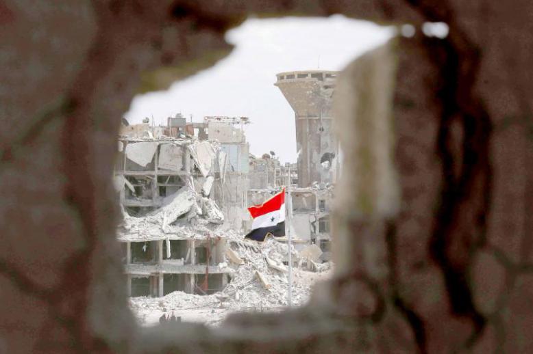 A Syrian flag flies in a rubble strewn street at the entrance of the Hajar al-Aswad neighbourhood on the southern outskirts of Damascus