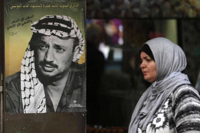 A Palestinian woman walks past a portrait of late leader Yasser Arafat in the West Bank city of Ramallah