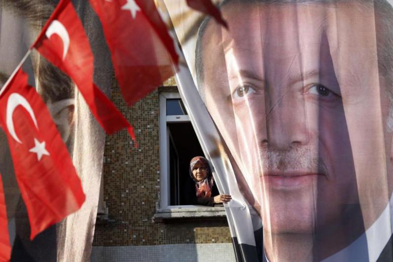 A woman peers out of her window behind a banner of Turkey’s President Recep Tayyip Erdogan in Istanbul, March 5