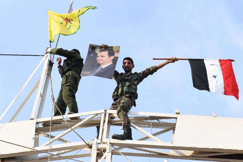 A Syrian government soldier holds up a portrait of President Bashar al-Assad and a Syrian national flag while another stands by a Kurdish YPG flag