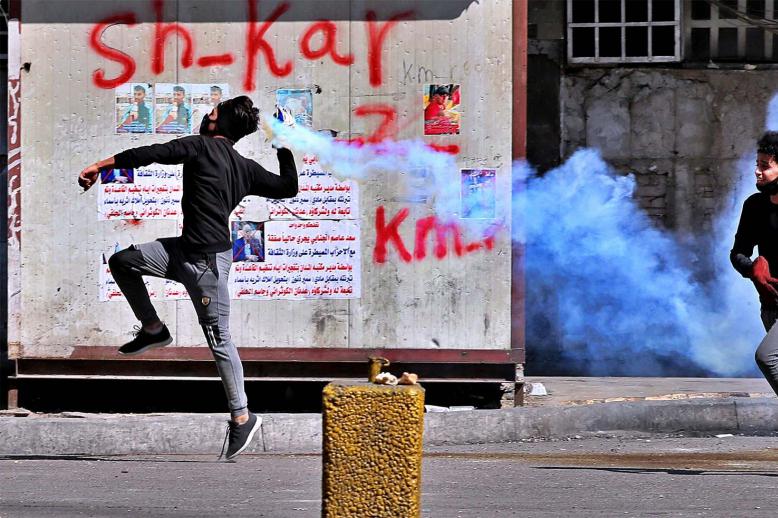 An anti-government protester prepares to throw back a tear gas canister fired by riot police, during clashes in Baghdad 