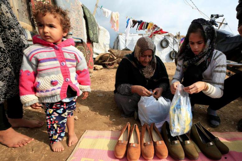 Syrian refugees hold bags of gloves for preventing the coronavirus' spread, in al-Wazzani area in southern Lebanon