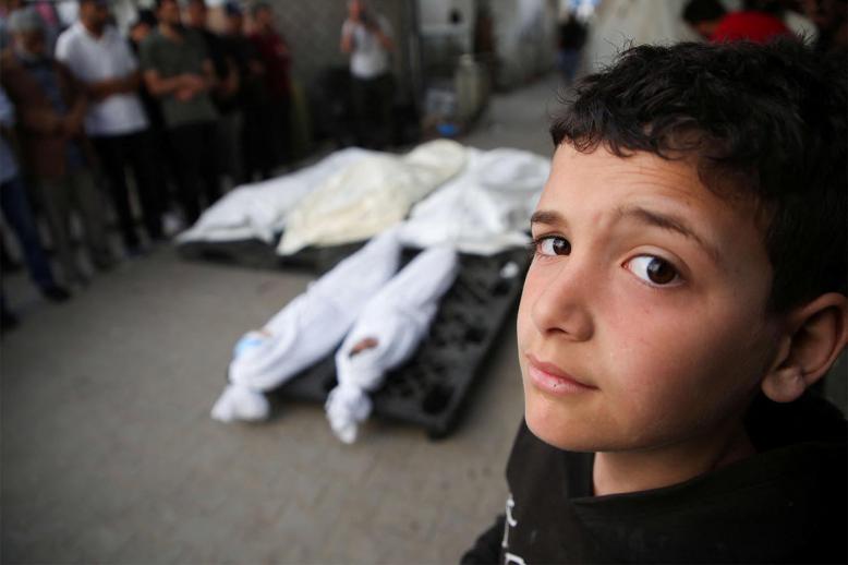A Palestinian boy stands next to the bodies of Palestinians killed in Israeli strike on Rafah