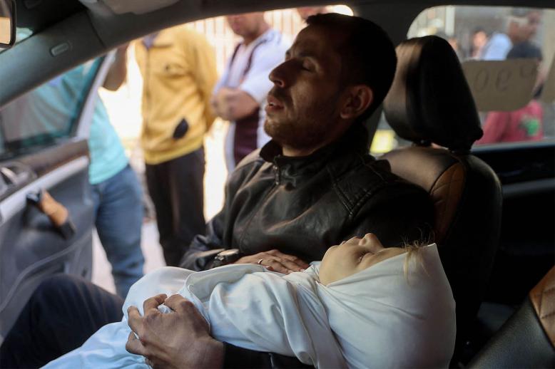 A Palestinian man sitting in a vehicle carries the body of a child killed in overnight Israeli airstrikes