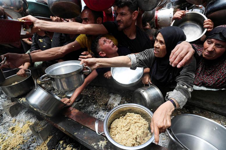 Palestinians wait to receive food cooked by a charity kitchen in Jabalia