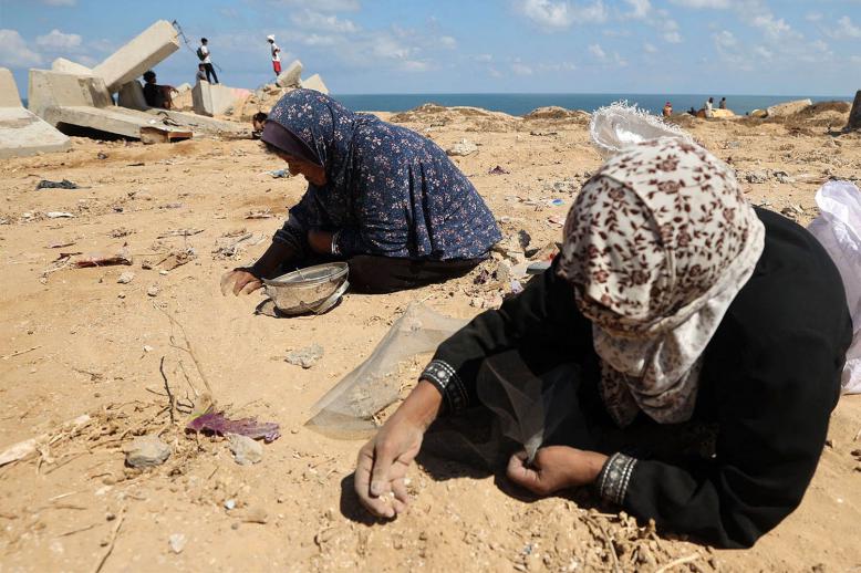 Palestinian women search the sand for legumes or rice in Nuseirat in Gaza Strip during an airdrop mission above the Israel-besieged Palestinian territory 
