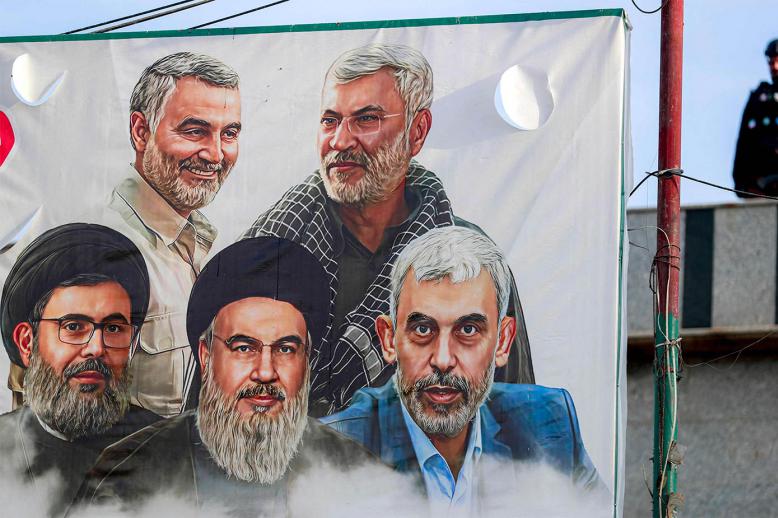 A member of the Iraqi security forces stands near a banner depicting figures of Iran-backed militant groups killed by Israel