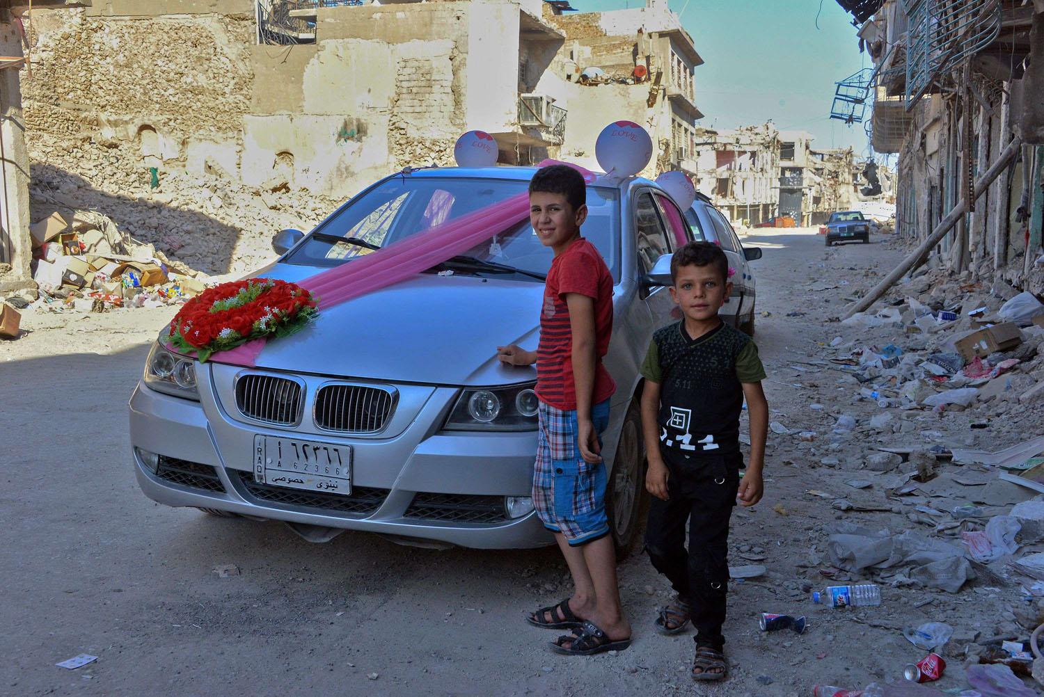 طفلان عراقيان أمام سيارة لعريس وعروسة وسط خراب الموصل