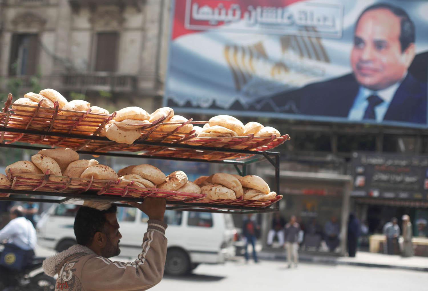 عامل يحمل خبزا يمر بالقرب من ملصق للرئيس المصري