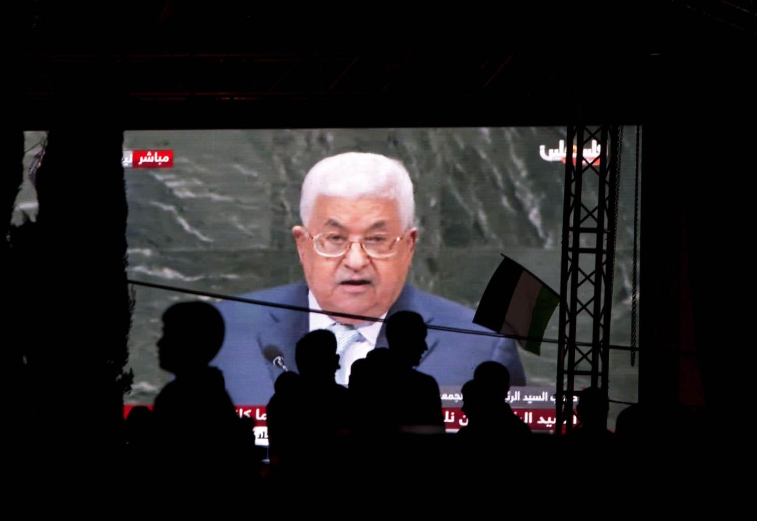فلسطينيون يتحدثون على خلفية شاشة تنقل خطاب الرئيس الفلسطيني عباس في الأمم المتحدة