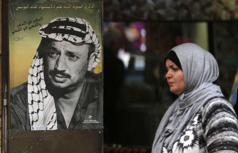 A Palestinian woman walks past a portrait of late leader Yasser Arafat in the West Bank city of Ramallah