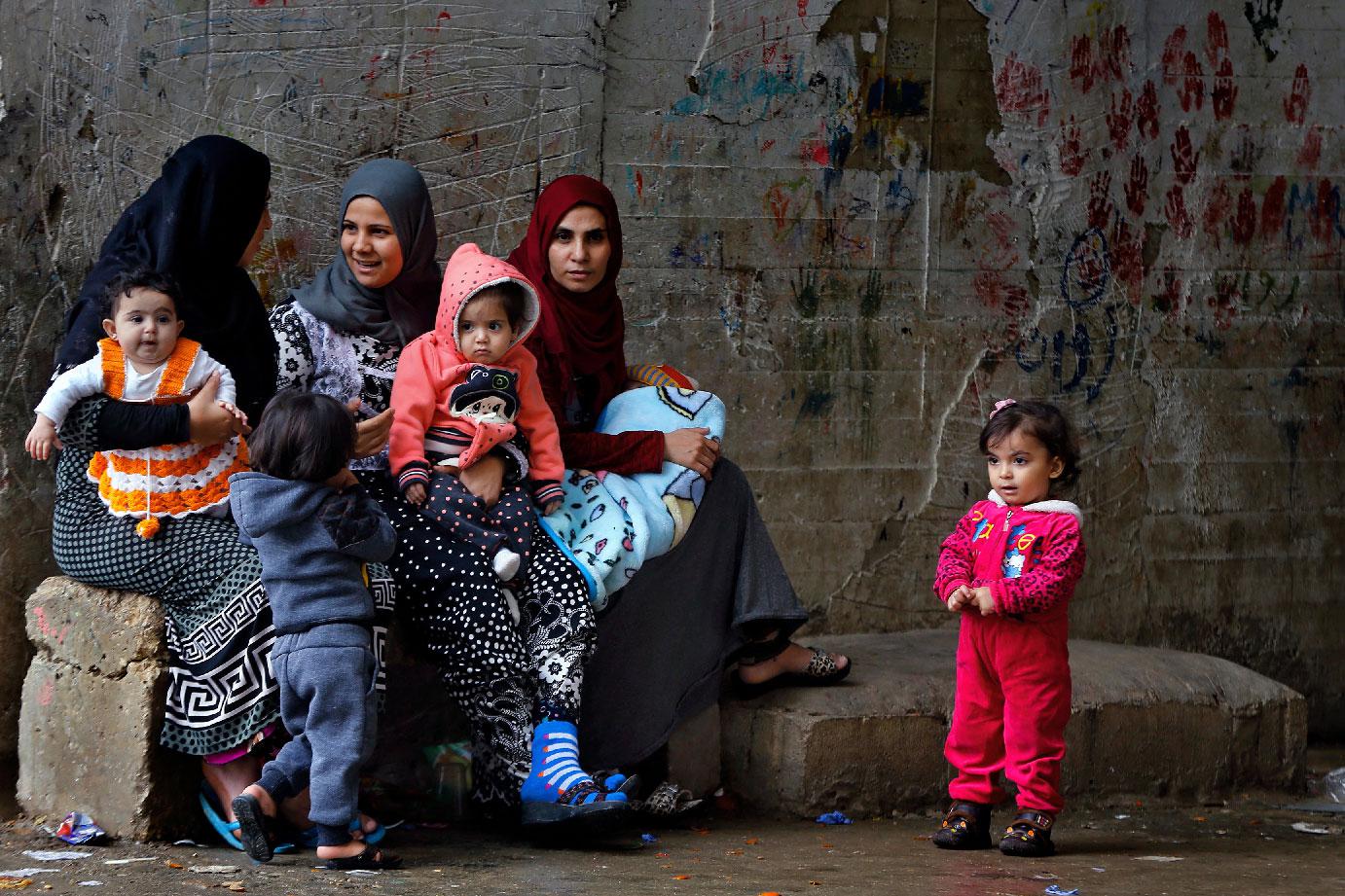 Syrian refugees women hold their children as they sit in Ouzai refugee compound, in the southern port city of Sidon, Lebanon. 