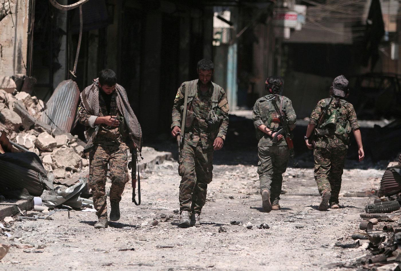 Syria Democratic Forces (SDF) fighters walk on the rubble of damaged shops and buildings in the city of Manbij.