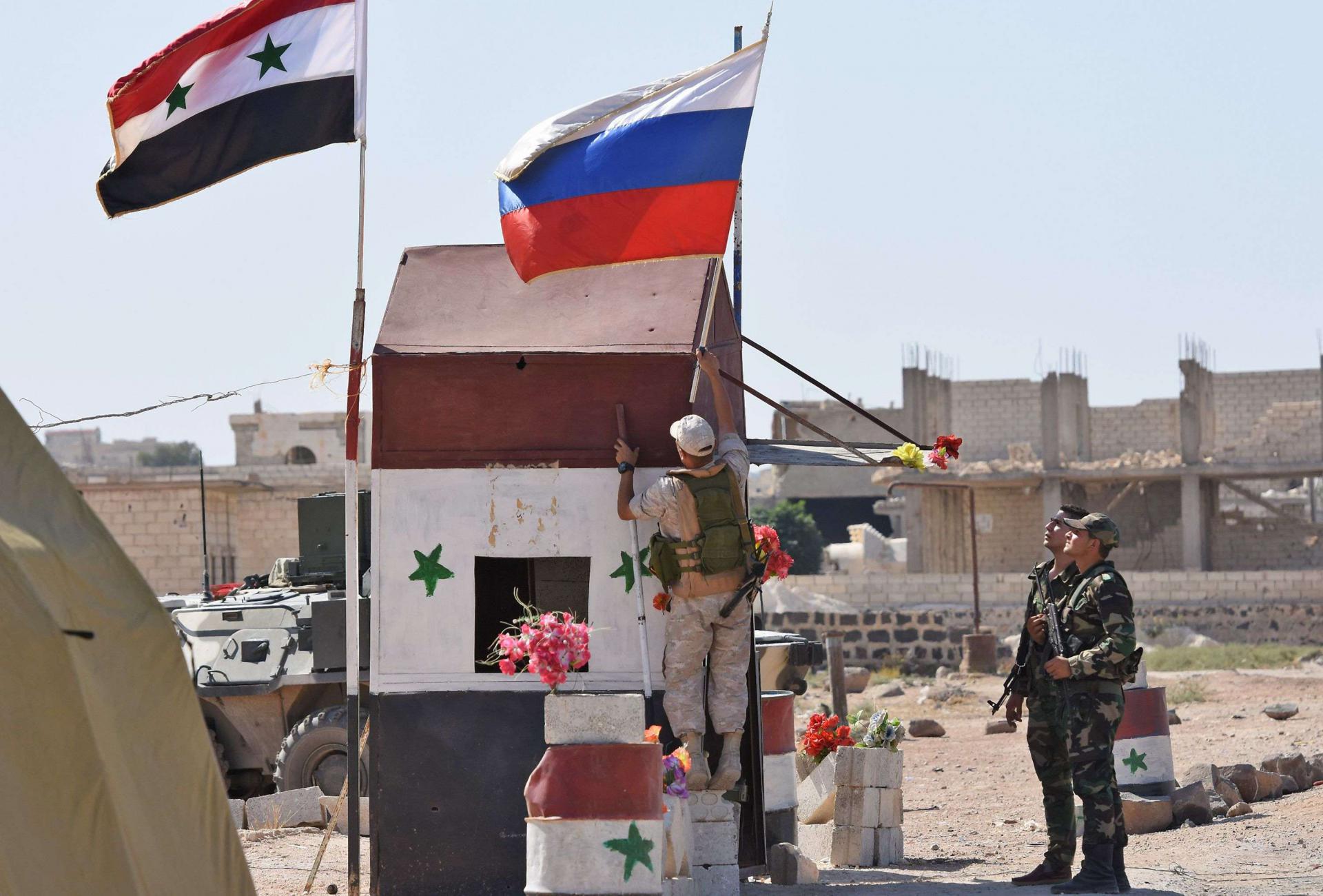 Russian soldiers place the national flag at the Abu Duhur crossing on the eastern edge of Idlib province on September 25, 2018, as Syrian families cross from rebel-held areas to regime-held areas.