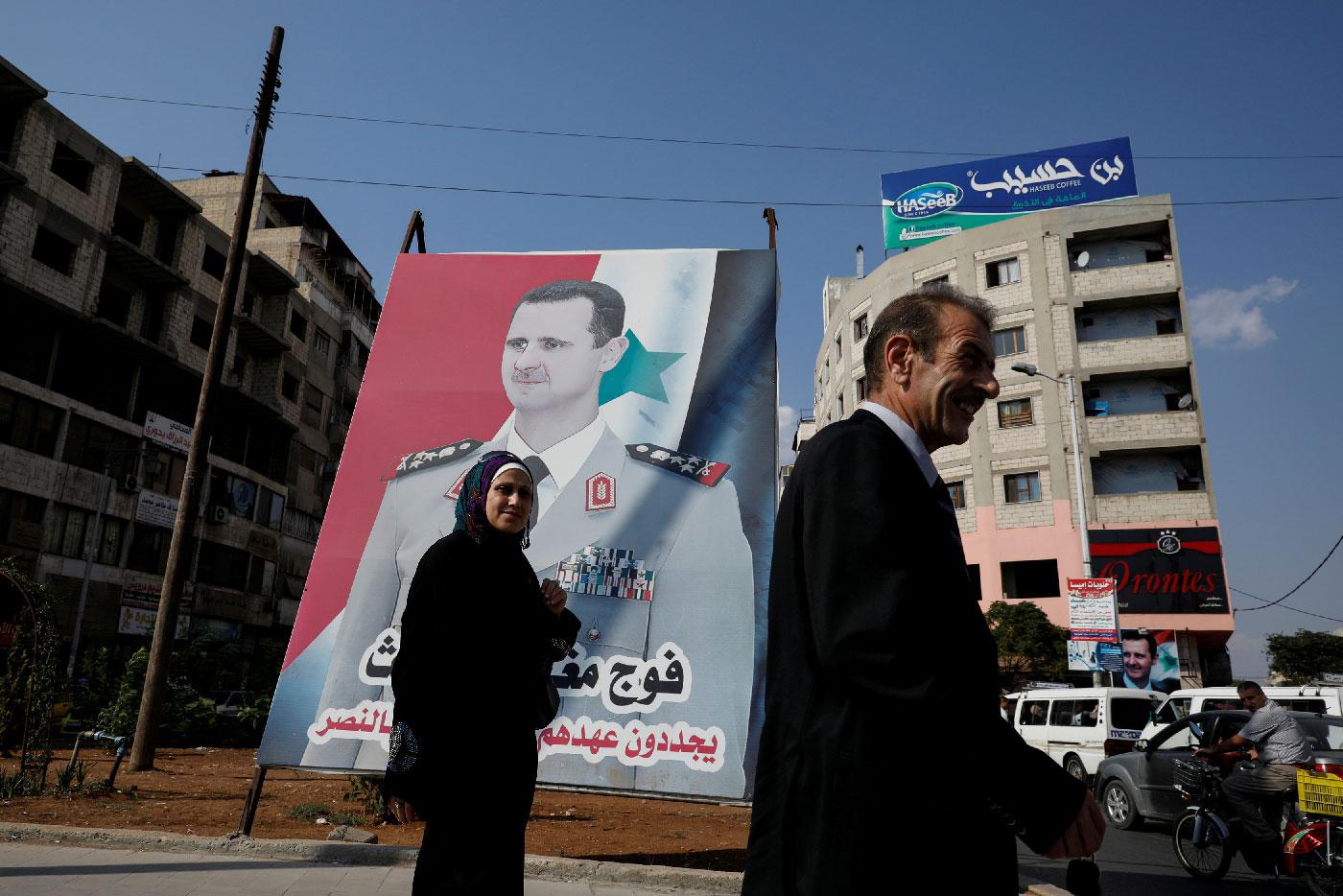 People walk in front of a billboard with a picture of Syrian President Bashar al-Assad in Homs, Syria, September 18, 2018.