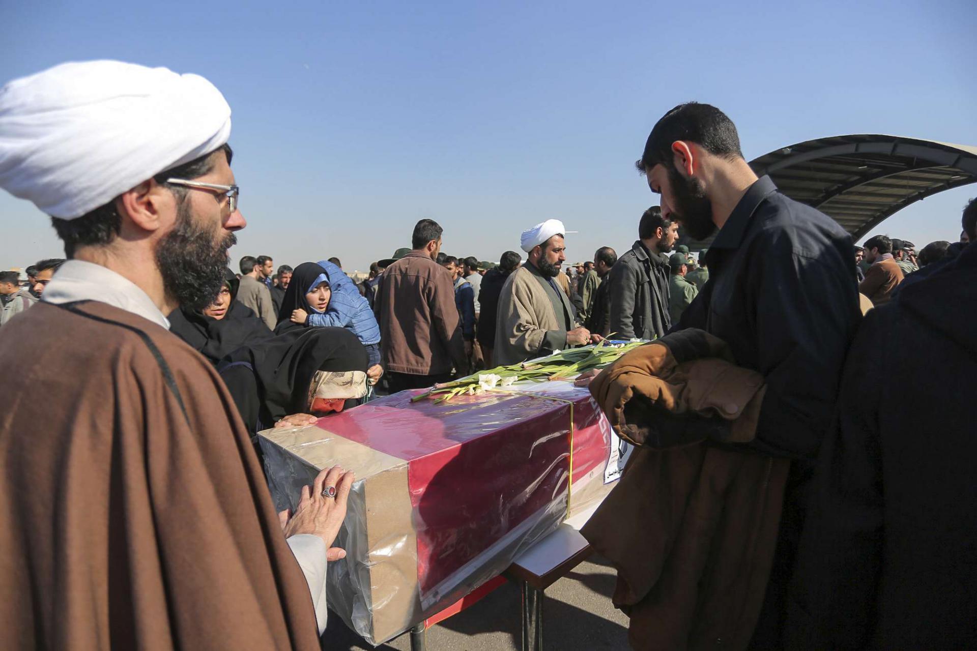 People mourn over a flag-draped coffin of a member of Iran's Revolutionary Guard who was killed in a suicide car bombing that struck a bus carrying the Guard troops, killing at least 27 people on Wednesday, upon arrival of the victims bodies and wounded troops at an airport in Isfahan, Thursday, Feb. 14, 2019.