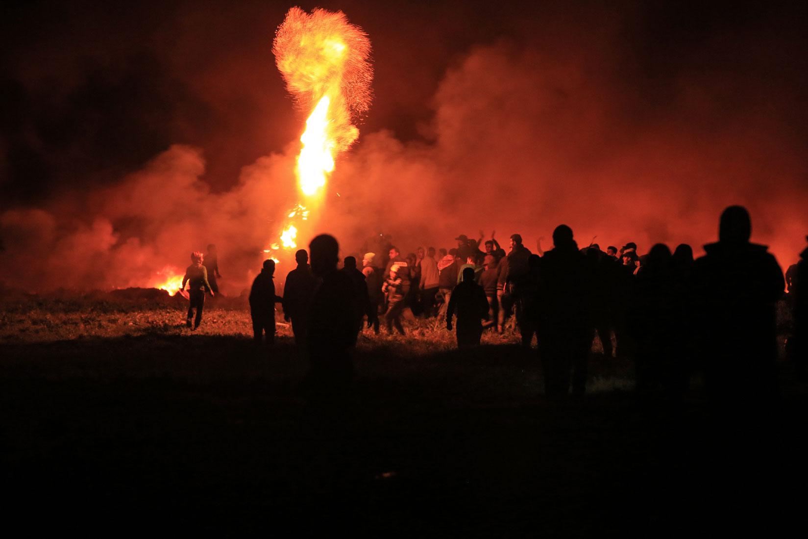 Palestinians watch as an object burns during night clashes between Palestinian demonstrators and Israeli security forces along the Israel-Gaza fence.